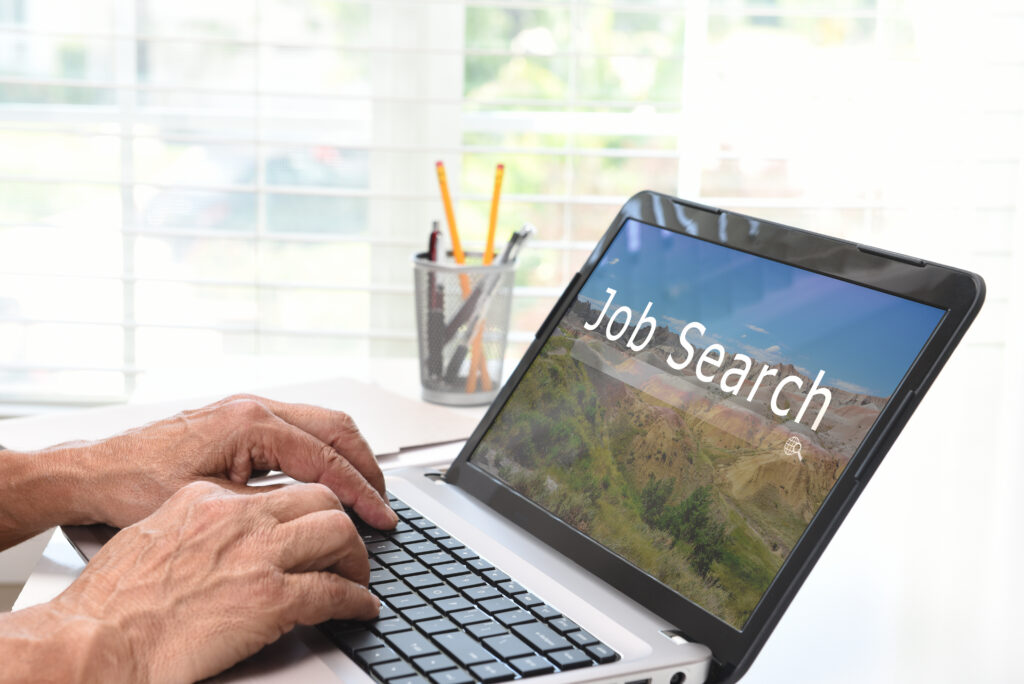 A person types on a laptop displaying a “job search” screen, capturing a focused moment of job hunting.